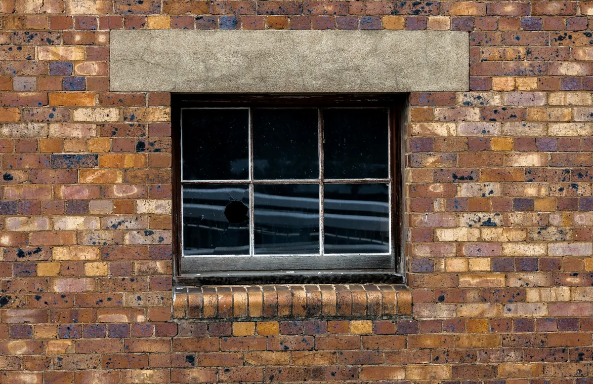 A weathered brick wall with a steel-framed window and a broken pane