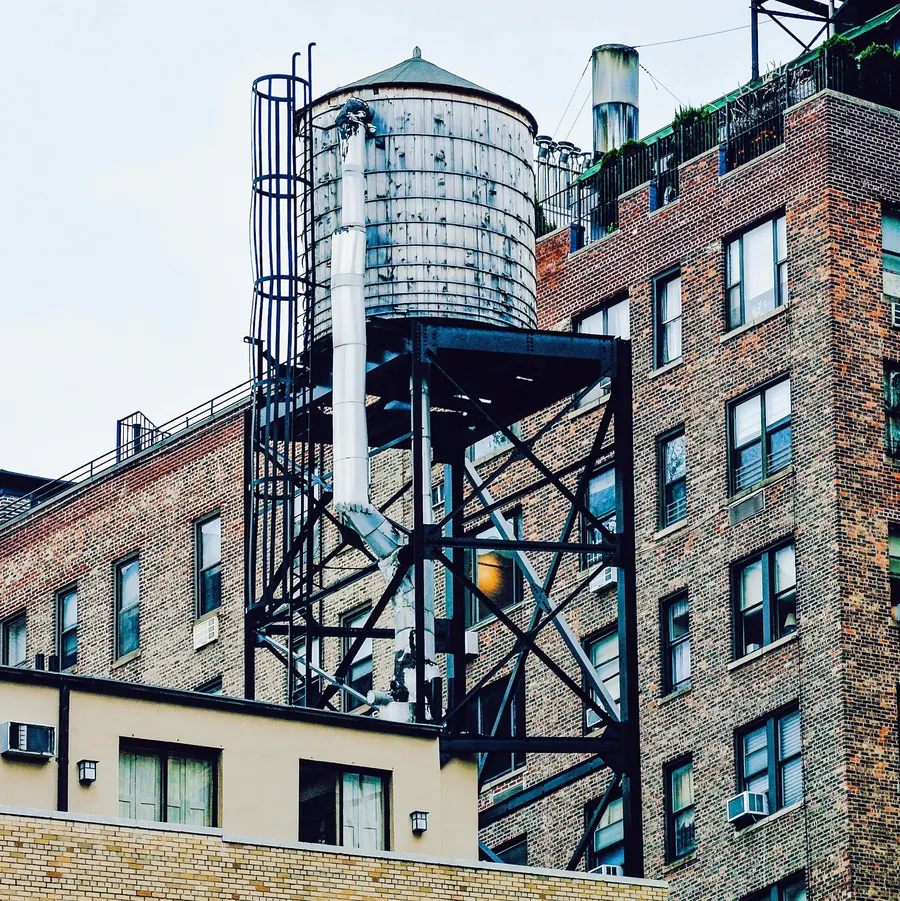 A rooftop water tank on a steel frame above a brick apartment building in New York